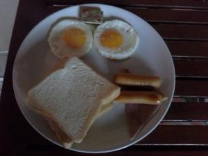 einen Teller mit einem Ei und einem Sandwich und Wurst in der Unterkunft Tamarind Grand Resort Mae Sariang in Mae Sariang