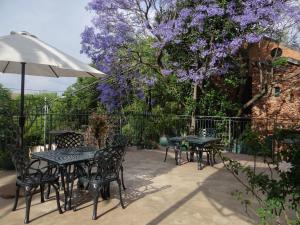 a patio with tables and chairs and a tree with purple flowers at Agterplaas Guesthouse in Johannesburg