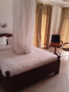 1 dormitorio con 1 cama con sábanas blancas y silla en Western Meridian Hotel Ltd Bushenyi, en Bushenyi