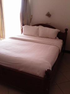 uma cama com lençóis brancos e almofadas num quarto em Western Meridian Hotel Ltd Bushenyi em Bushenyi