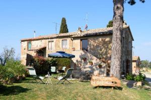 uma casa com cadeiras, um guarda-sol e uma árvore em Antico Podere la Martinella em San Quirico dʼOrcia