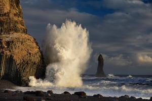 a large wave hitting the beach with two large rocks at Hótel Kría in Vík