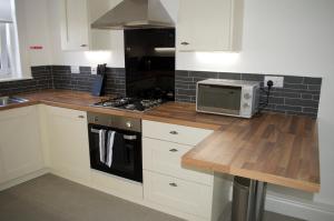 cocina con armarios blancos, fogones y microondas en Maze Serviced Apartment, en Ayr