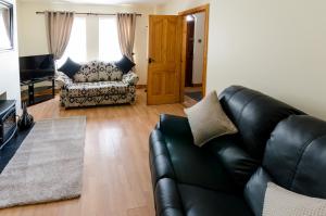 sala de estar con sofá de cuero y silla en fairhill holiday let, en Ballycastle