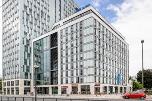 un gran edificio blanco con un coche rojo delante de él en ibis budget Berlin Alexanderplatz en Berlín