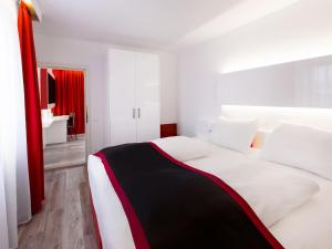 a bedroom with a white bed with a red curtain at DORMERO Hotel Burghausen in Burghausen