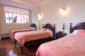 a bedroom with three beds with pink sheets and a window at Hotel Europa in Alausí