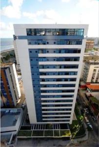 a tall white building with blue windows next to the ocean at Studio Everest By Smart Stays in Recife