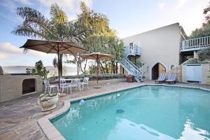 a swimming pool with an umbrella and a house at Paradise View Apartment in Knysna