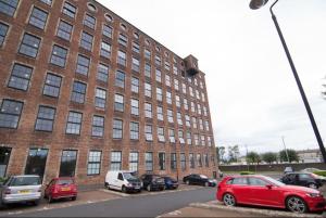 een groot bakstenen gebouw met auto's geparkeerd voor het bij Loft Apartment in Port Glasgow