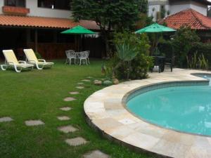 una piscina en un patio con sillas y sombrillas en Pousada Praia de Itacoatiara en Niterói