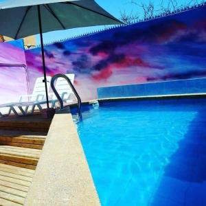 a swimming pool with an umbrella and a mural at Aotea Hostel Iquique in Iquique