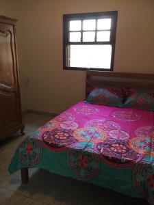 a bedroom with a bed with a pink bedspread and a window at Vila Colorida casa 2 in Fazendinha