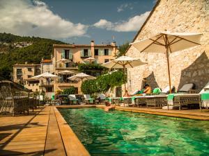 a swimming pool with umbrellas and people sitting on chairs at Auberge De Tourrettes in Tourrettes-sur-Loup