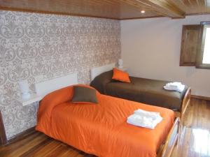 two beds with orange sheets in a room at Casa Saleta in Melide