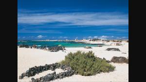 a sandy beach with people in the water and the ocean at casa orymar in El Cotillo