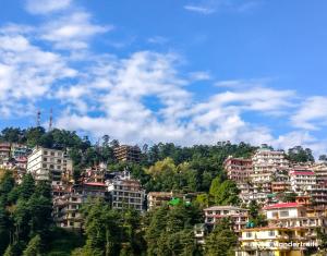 eine Gruppe von Gebäuden auf einem Hügel mit blauem Himmel in der Unterkunft Himalayan Homestay in Dharamshala