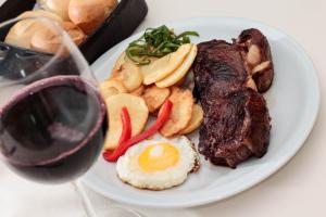 a plate of steak and eggs and potatoes with a glass of wine at Condado Hotel Casino Santo Tome in Santo Tomé
