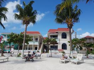 people sitting on chairs in front of a building with palm trees at Jan's Hotel in Caye Caulker