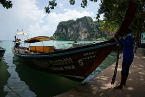 a man standing next to a boat in the water at Sand Sea Resort Railay Beach in Railay Beach