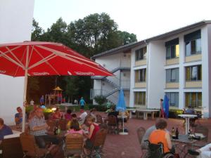 un grupo de personas sentadas en sillas bajo un paraguas rojo en HI Munich Park Youth Hostel, en Múnich