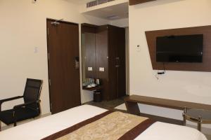 a bedroom with a bed and a tv and a chair at Hotel Grand Gayathri in Khammam