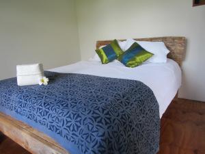 a bed with a blue and white comforter and green pillows at Mulberry Grove Retreat in Tryphena