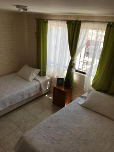 バイーア・イングレサにあるBahia Inglesa Apartamentosのベッドルーム1室(ベッド2台付)、緑のカーテン付きの窓が備わります。