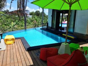 a swimming pool with a green umbrella and chairs at Villa Nitras in Canggu