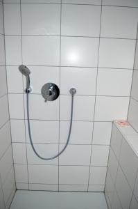 a shower with a hose in a white tiled bathroom at Beim Hooch "Schindelloft" in Brücktal