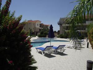 a swimming pool with two lounge chairs and an umbrella at Pyla Gardens A102 in Pyla
