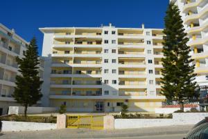 un grand bâtiment blanc avec des arbres devant lui dans l'établissement Apartamento Estrela do Mar a 50 metros da praia, à Armação de Pêra