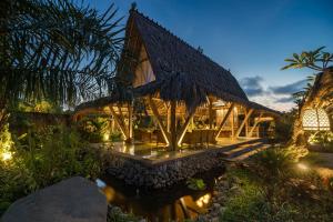 a house with a thatched roof and a pond at Arya Villas Ubud in Ubud