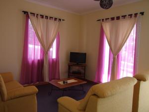 ein Wohnzimmer mit rosa Vorhängen sowie einem Tisch und Stühlen in der Unterkunft Paraiso das Flores in Estreito da Calheta