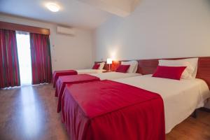 two beds in a hotel room with red sheets at Hotel Cristo Rei - Fatima in Fátima