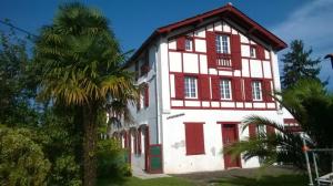 un gran edificio blanco y rojo con una palmera en Agréable appartement à CAMBO LES BAINS, en Cambo-les-Bains