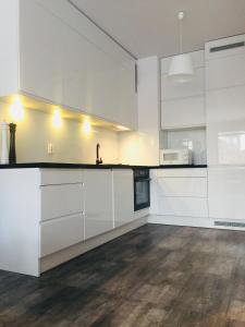 a kitchen with white cabinets and a wooden floor at Apartament Aquarius Sopot in Sopot