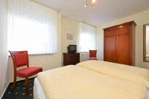 a bedroom with two beds and a chair and a television at Nordseegartenpark Nordseestolz in Bensersiel