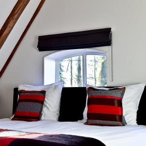 a bed with red and black pillows and a window at De Woeste Wieven op Erve Bonkert in Diepenheim