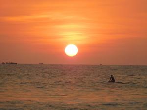 a person riding a surfboard in the ocean at sunset at Our World Mirissa in Mirissa