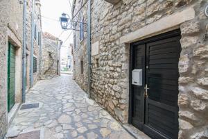 an alley with a black door on a stone building at Old Town House Pakoštane in Pakoštane