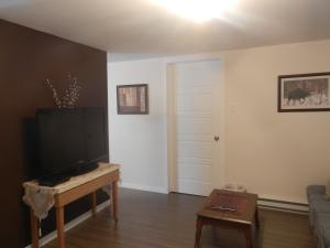 a living room with a flat screen tv and a table at Gite La Ptite Falaise hébergement touristique in Sainte-Anne-des-Monts