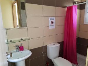 a bathroom with a toilet sink and a pink shower curtain at Mazotos Panoramic Village in Mazotos