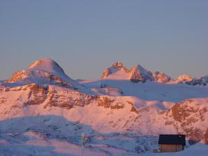 einen schneebedeckten Berg mit einem Haus im Vordergrund in der Unterkunft Dormio Gasthof Höllwirt in Obertraun