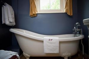 a white bath tub in a blue bathroom with a window at Ravenwood Hall Hotel in Bury Saint Edmunds +29 photos