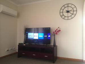 a flat screen tv sitting on a cabinet with a clock at Home & Away St Leonards in Saint Leonards
