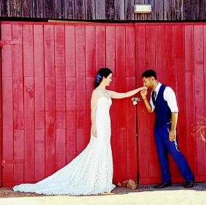 Una novia y un novio parados frente a un granero rojo en Red Door Collective - RDC Vineyard Estate, en Pokolbin