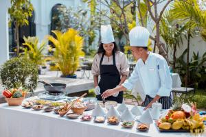 Ein Mann und eine Frau stehen neben einem Tisch mit Essen. in der Unterkunft Sarai Resort & Spa in Siem Reap