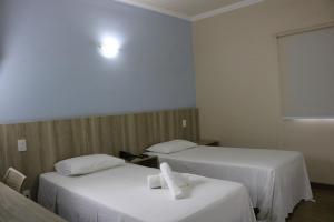 2 camas en una habitación de hotel con sábanas blancas en Hotel Jaguar, en Uberaba