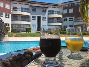 two glasses of beer sitting on a table near a swimming pool at Casa do Chico Cond Golden Dunas in Extremóz